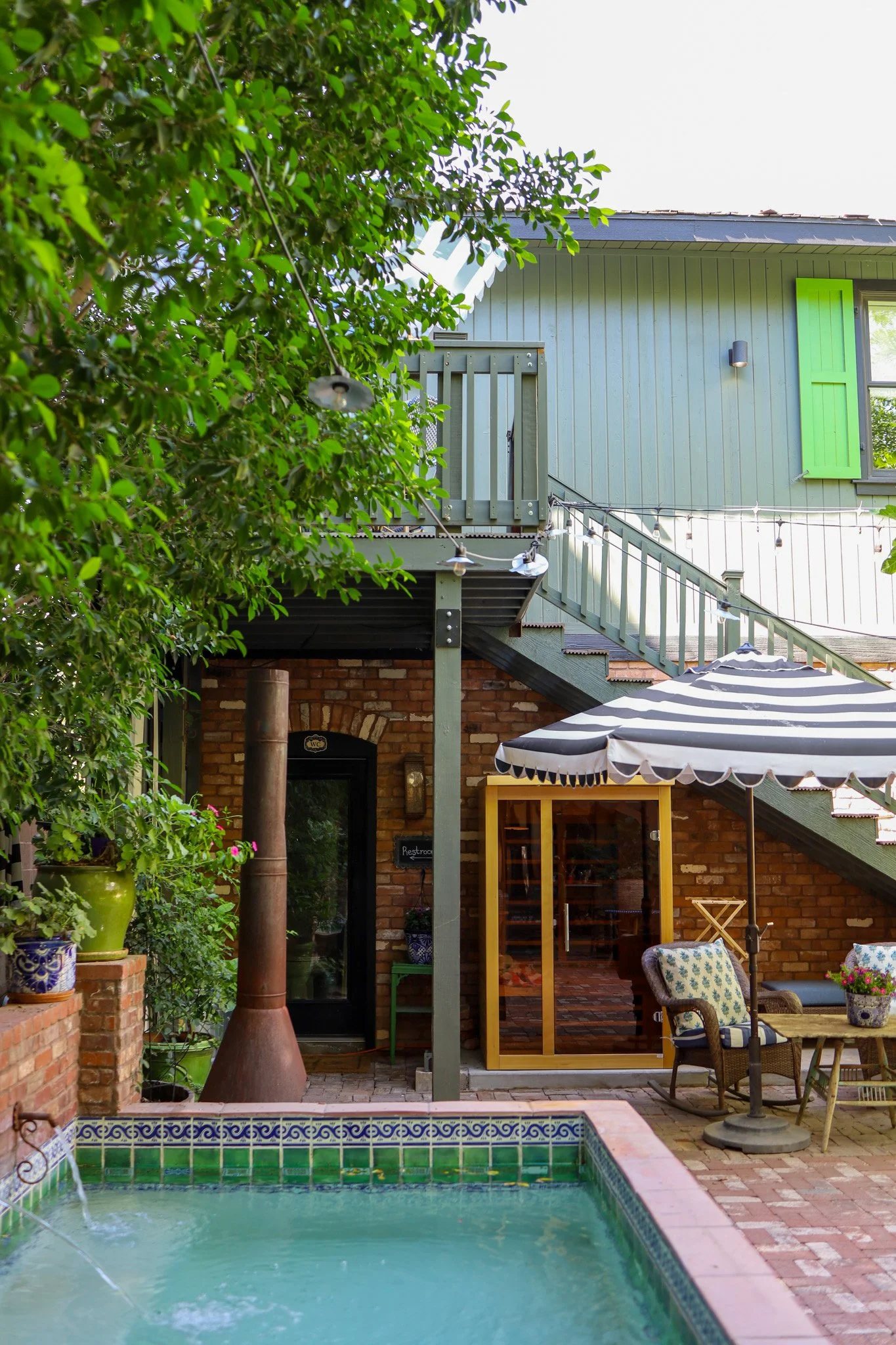 The courtyard at Boho Farm + Home: a tiled plunge pool, brick patio and a striped umbrella under the trees